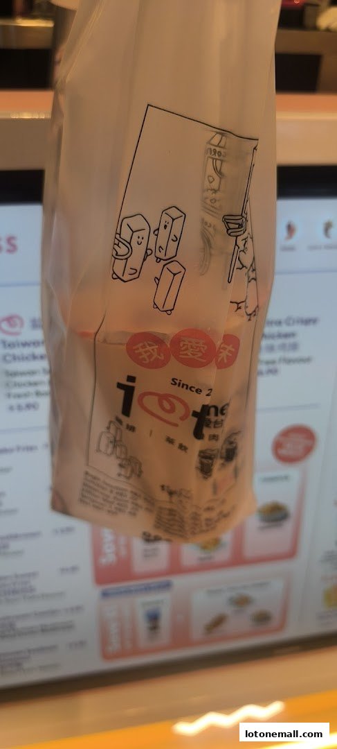 A branded paper bag with cartoon characters and text hangs in front of a blurred menu display.
