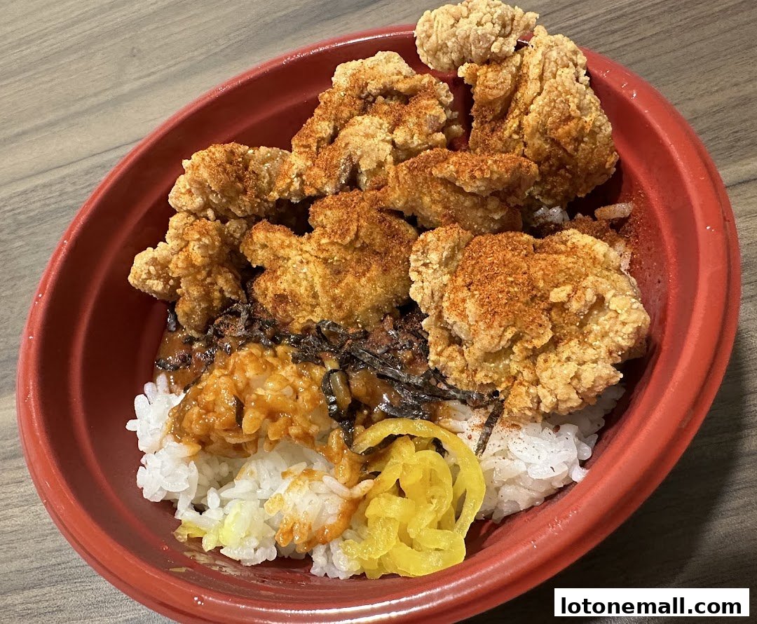 A close-up of a Japanese rice bowl with fried chicken, sauce, and pickled vegetables.