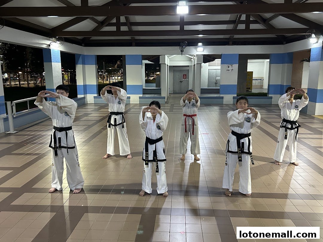 Children in Taekwondo uniforms practice martial arts poses outdoors.