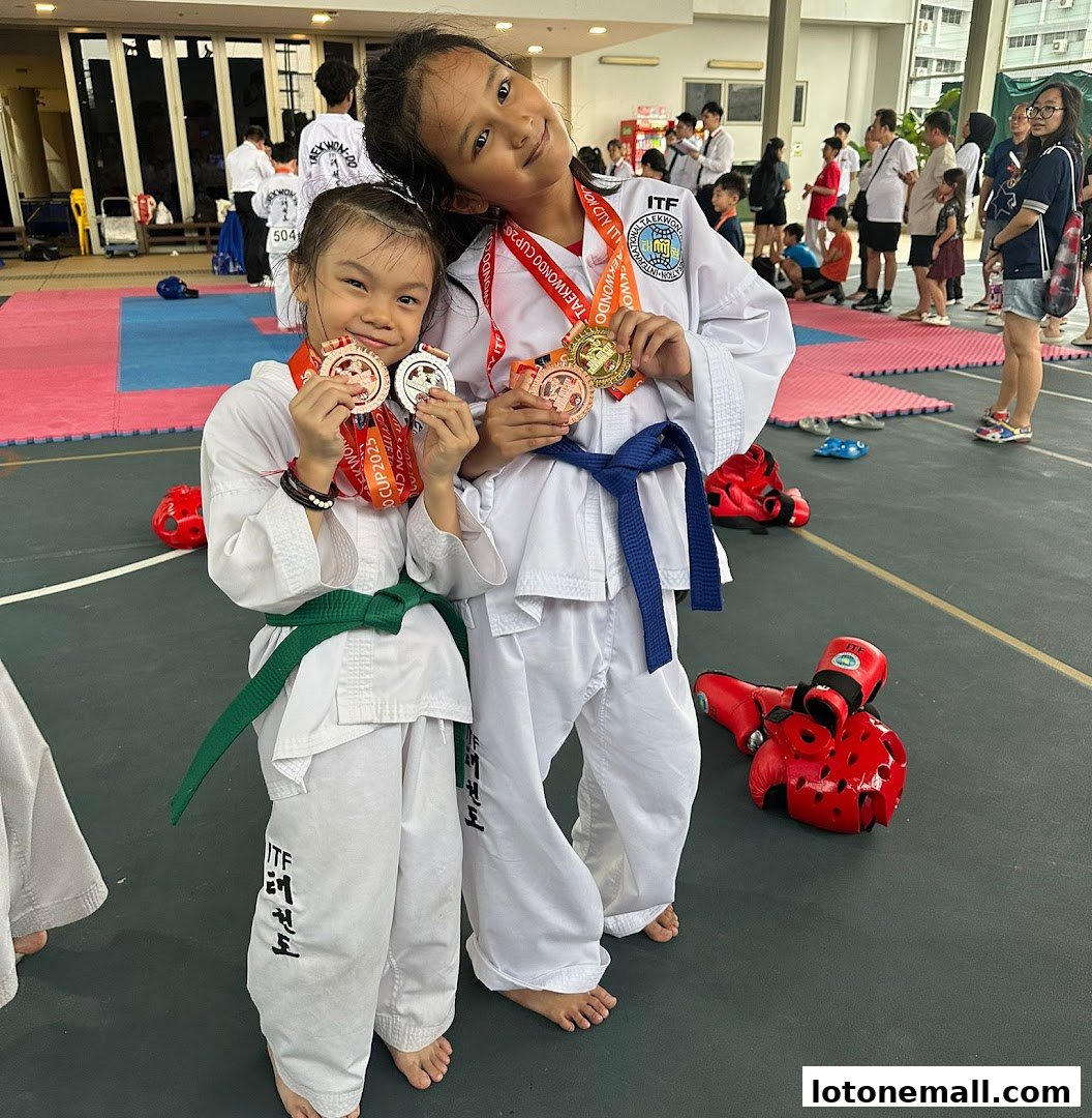 Two young girls in Taekwondo uniforms proudly display their medals after a competition.