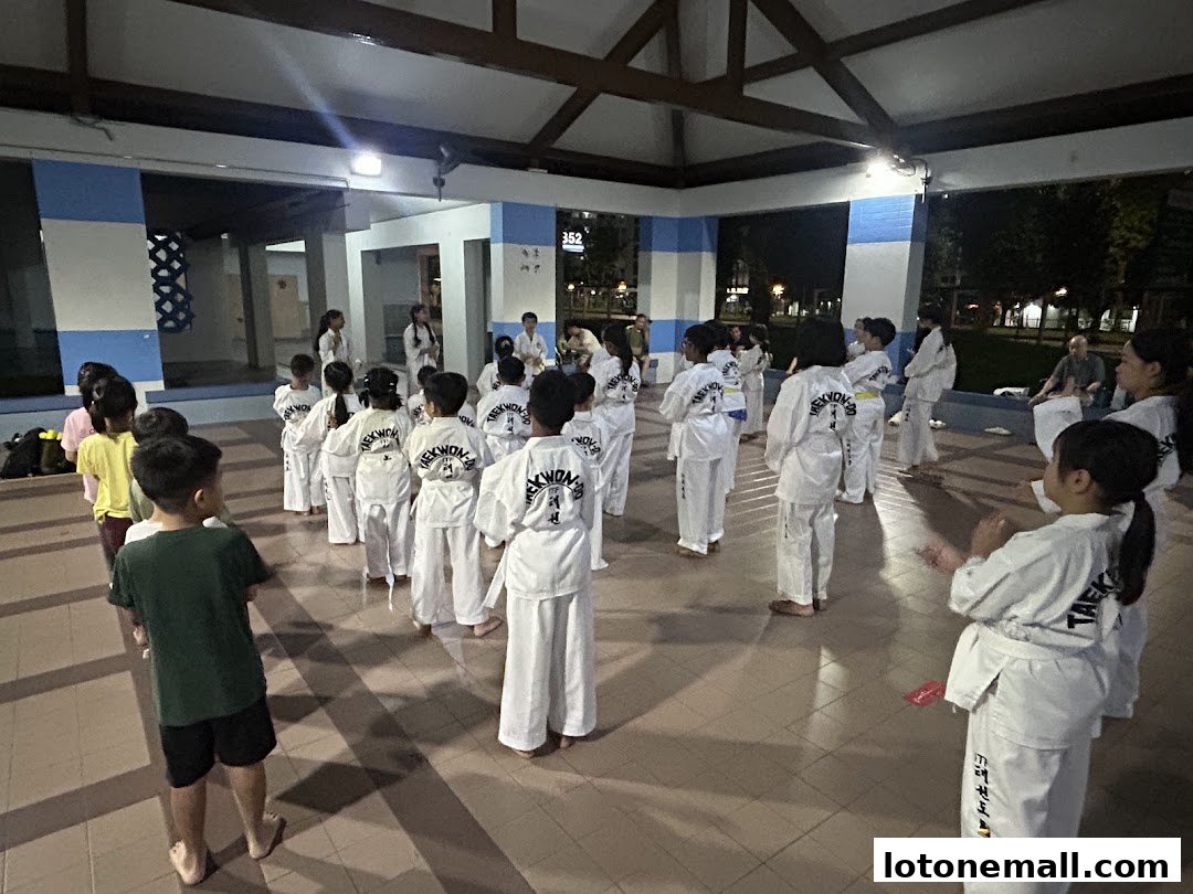 Children in Taekwondo uniforms practice in an outdoor covered area.