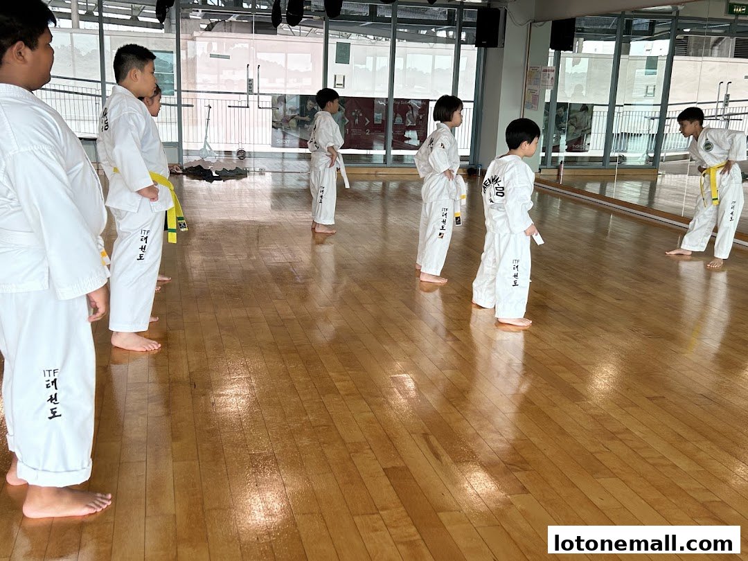 Children in Taekwondo uniforms practice in a studio with a large mirror.