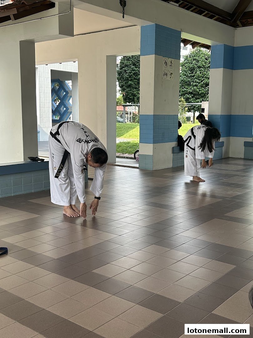 People in Taekwondo uniforms stretching indoors.