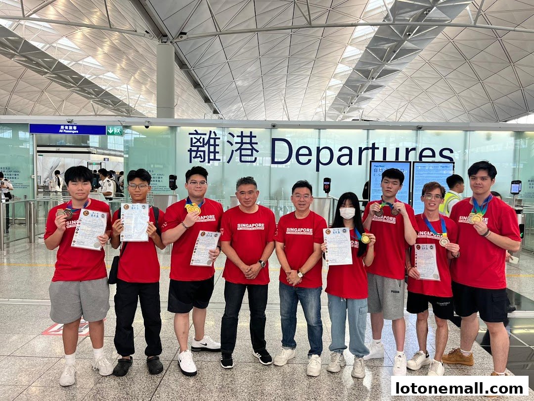 A group of people in red shirts with medals and certificates stand in front of a departures sign.