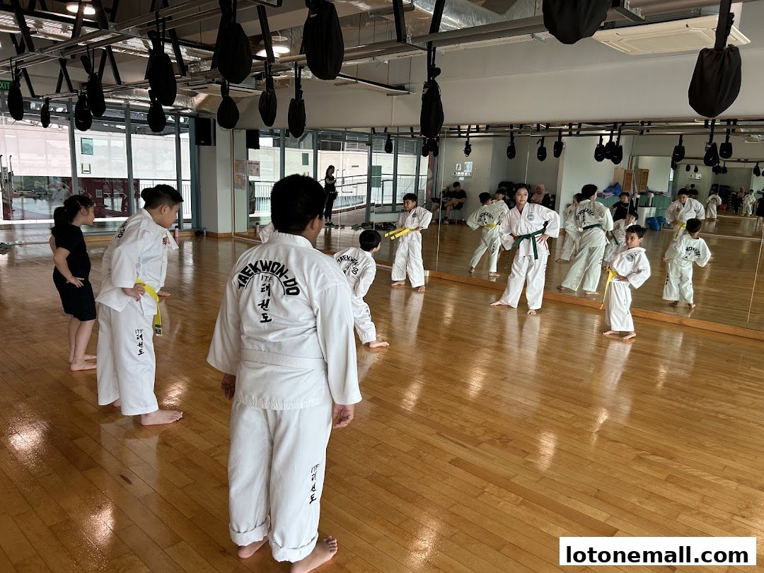 Children and adults practicing Taekwondo in a studio with mirrors and punching bags.