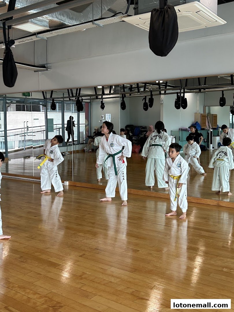 Children in Taekwondo uniforms practicing in a studio with a large mirror.