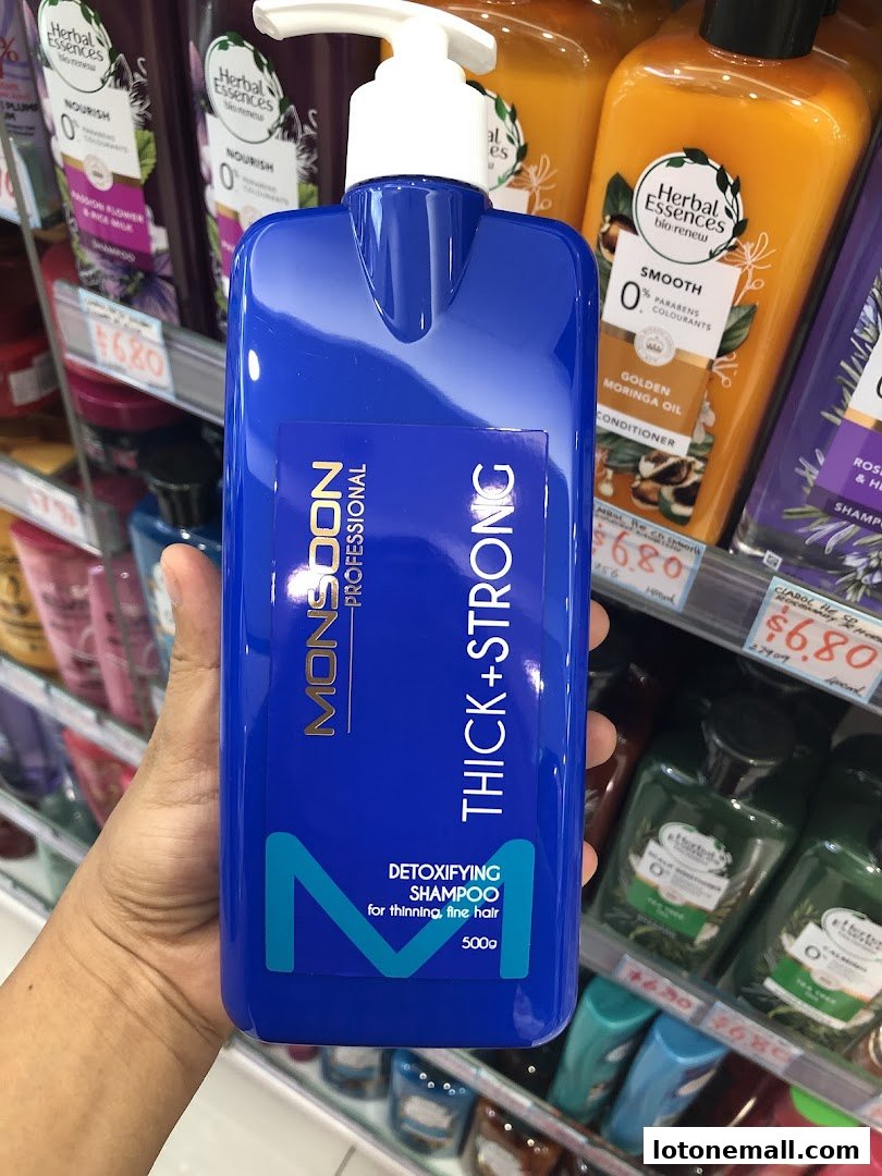 A hand holds a blue bottle of Monsoon Professional Thick+Strong Detoxifying Shampoo.