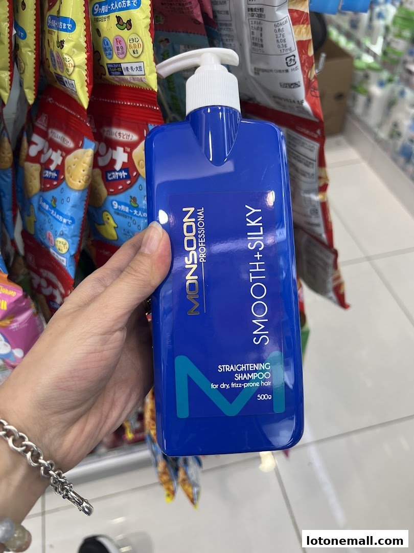 A hand holds a blue bottle of Monsoon Professional Smooth+Silky Straightening Shampoo.