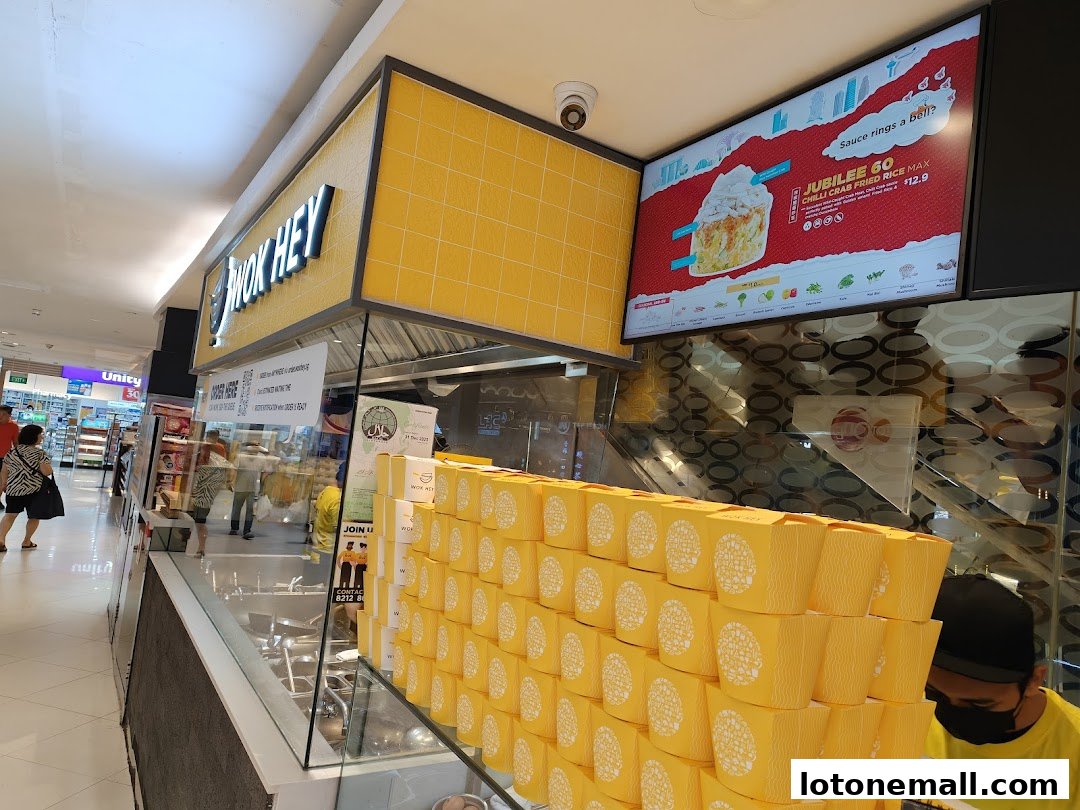 A Wok Hey food stall with bright yellow packaging and a digital menu board displaying a special offer.