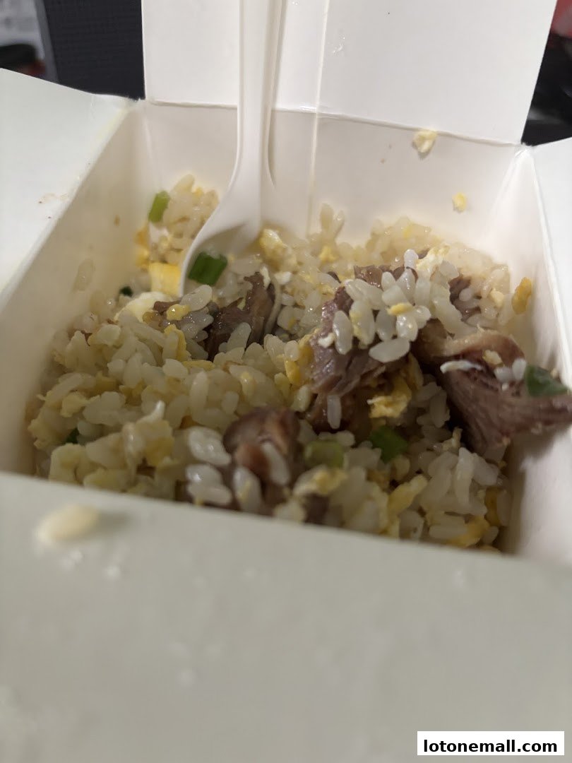 A close-up shot of a white takeout box filled with fried rice and meat.