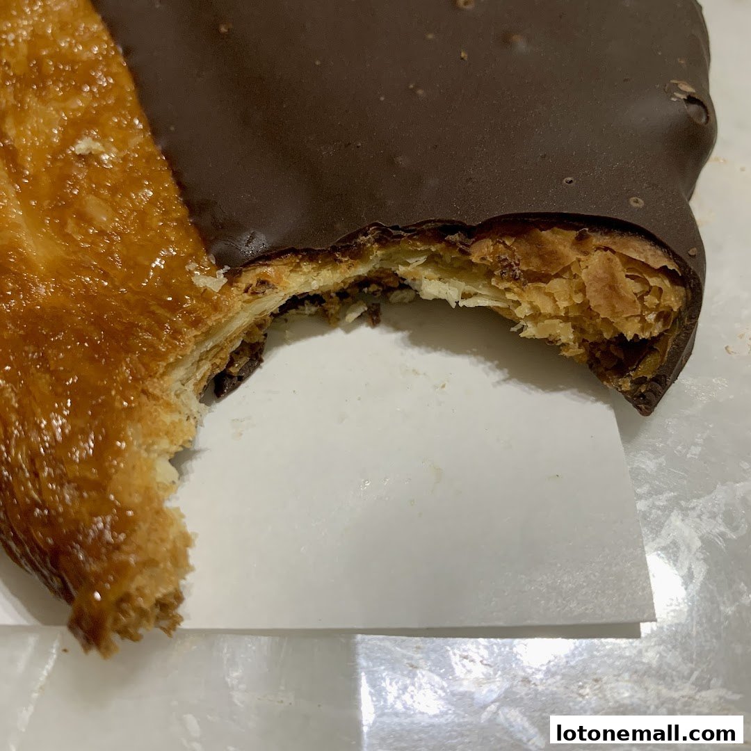 A close-up of a flaky pastry with chocolate icing, partially eaten.