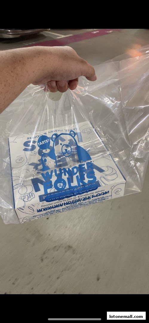 A hand holds a clear plastic bag containing a white box with blue lettering and cartoon bears.