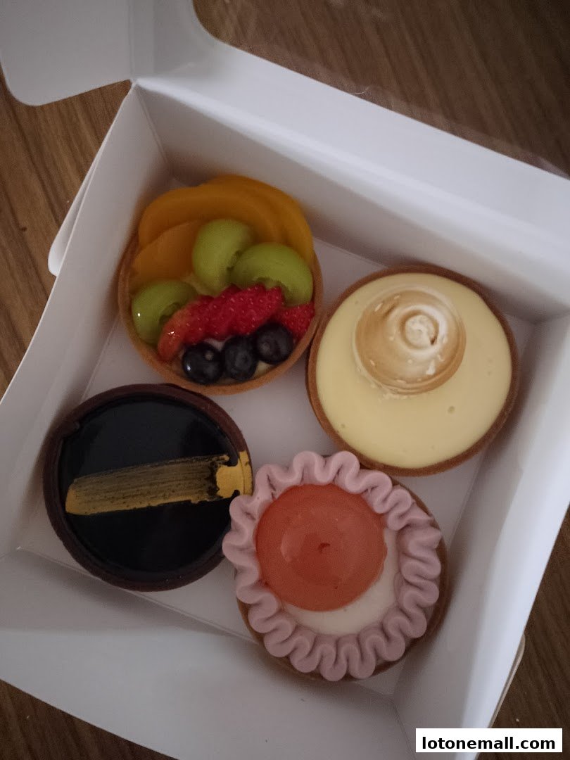 A white box containing four assorted handmade tarts with various fruit and cream toppings.