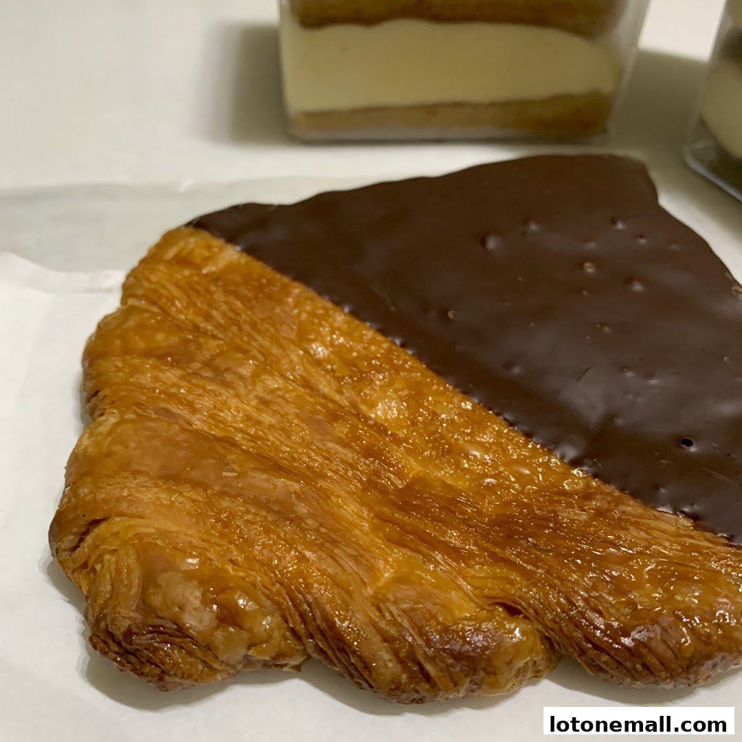 A close-up of a flaky pastry, half-dipped in rich chocolate.