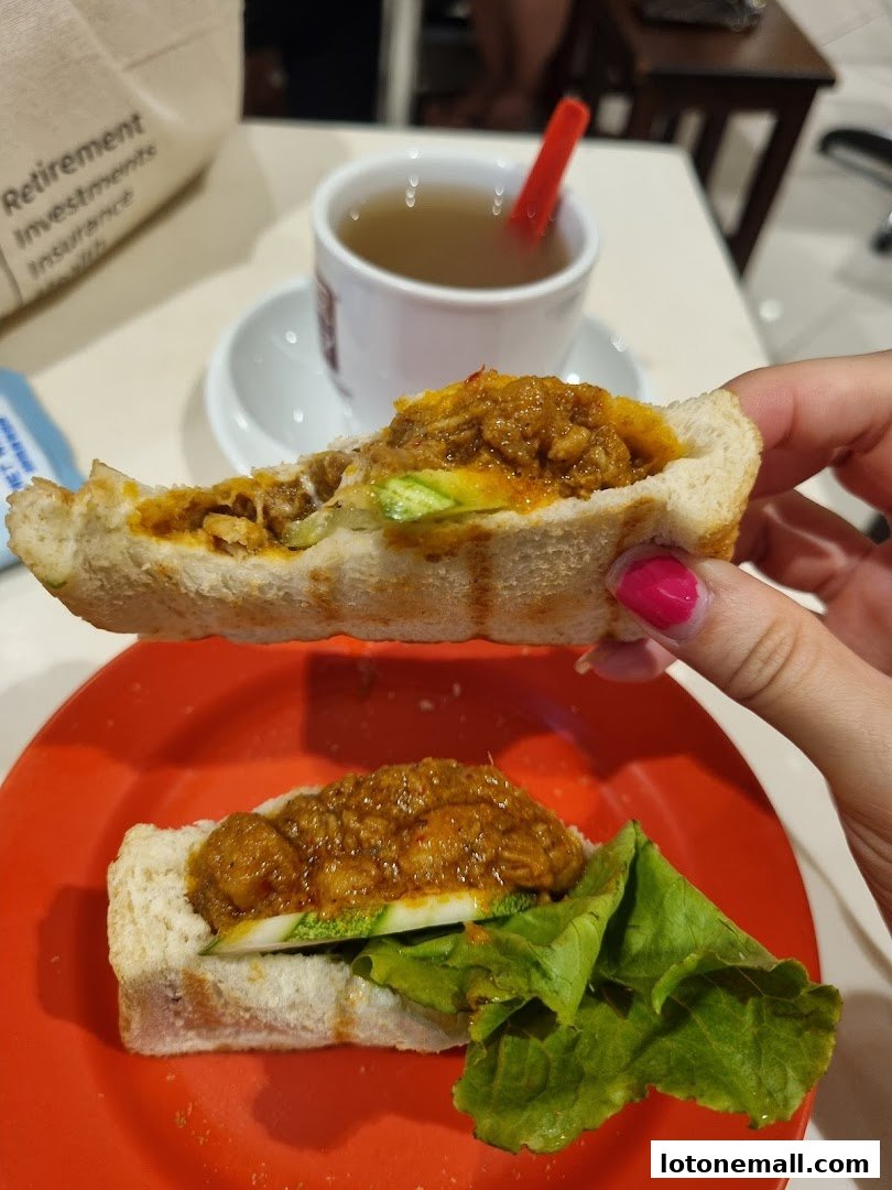 A person holds a kaya toast sandwich with a cup of tea in the background.