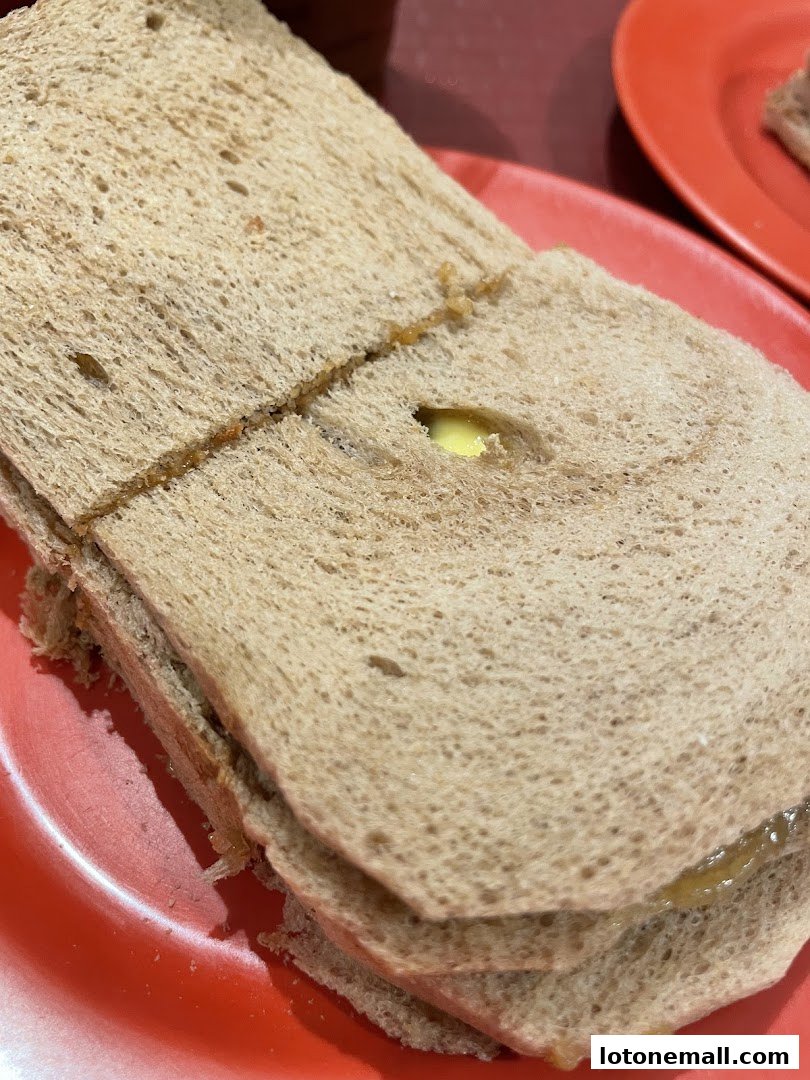 A close-up of a kaya toast sandwich with butter on a red plate.