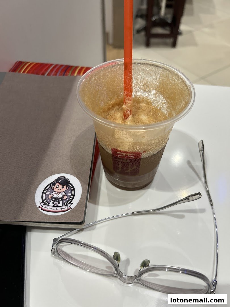 A cup of iced coffee with a straw, glasses, and a notebook on a table.