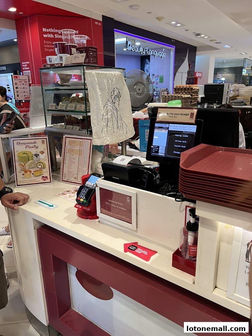 A counter at Ya Kun Kaya Toast with pastries, a POS system, and operating hours sign.