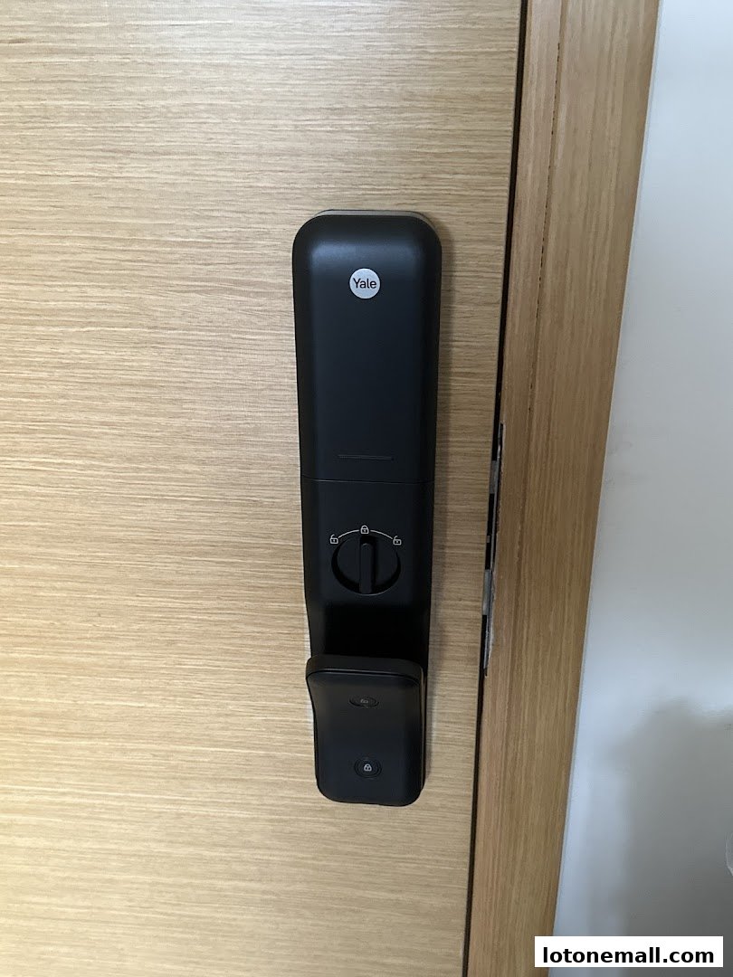 A close-up view of a black Yale smart lock installed on a light wood door.