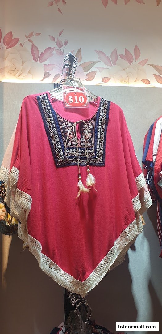A pink poncho with fringe and embroidered details is displayed on a hanger.