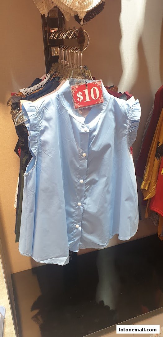 A light blue collared shirt with white buttons and ruffled sleeves is displayed on a hanger.