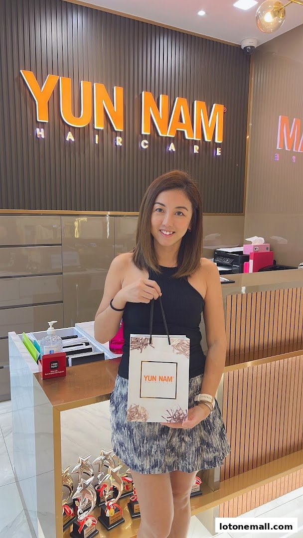 A woman holds a Yun Nam Hair Care shopping bag in front of the salon's reception area.