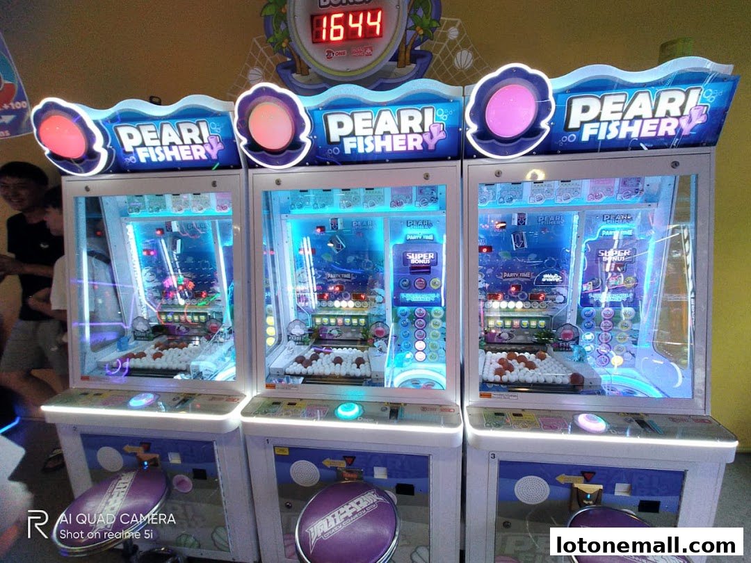 Three brightly lit "Pearl Fishery" arcade machines with purple seats in front.