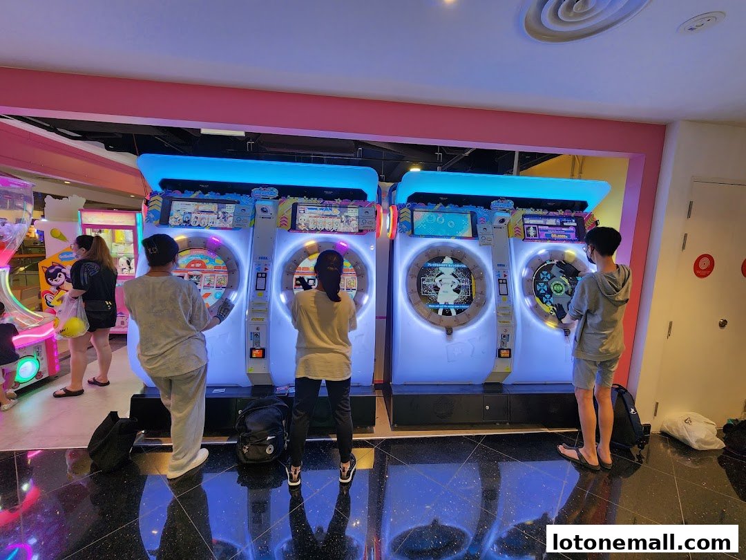 People playing rhythm games on colorful arcade machines in a brightly lit entertainment center.